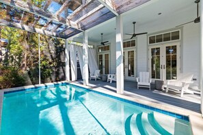 A poolside area with a clear blue pool, white lounge chairs, and a covered patio with glass ceiling. - Screened-in Pool, LSV/Golf Cart, & Bikes! Carriage House! Walk to Beach! (Santa Rosa Beach)