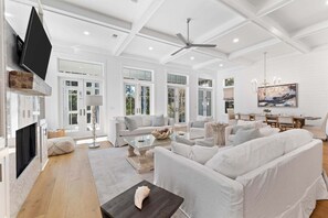 A spacious living room with white sofas, a glass coffee table, and a fireplace. - Screened-in Pool, LSV/Golf Cart, & Bikes! Carriage House! Walk to Beach! (Santa Rosa Beach)