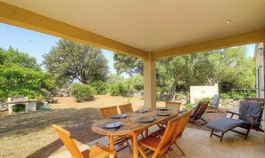 An outdoor patio with a wooden table and chairs, surrounded by greenery and a stone wall. - Villa Pierre - FIGARI (FIGARI)