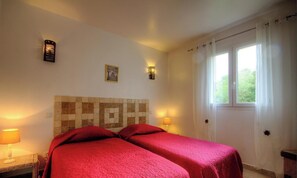 A room with two beds, a tiled headboard, two wall-mounted lamps, a window with curtains, and a picture on the wall. - Villa Pierre - FIGARI (FIGARI)