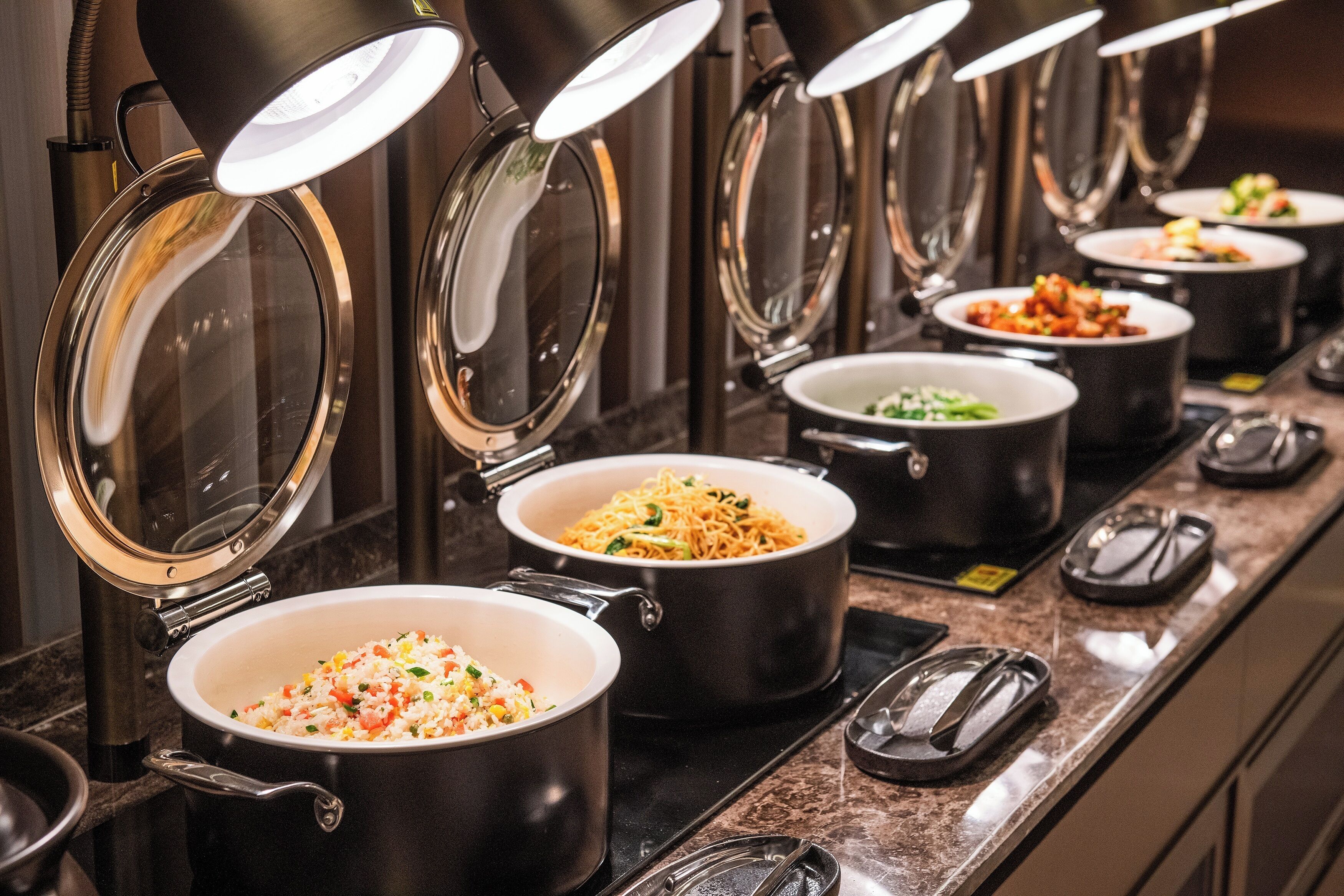 A buffet with multiple pots of food, each with a lid, on a counter.