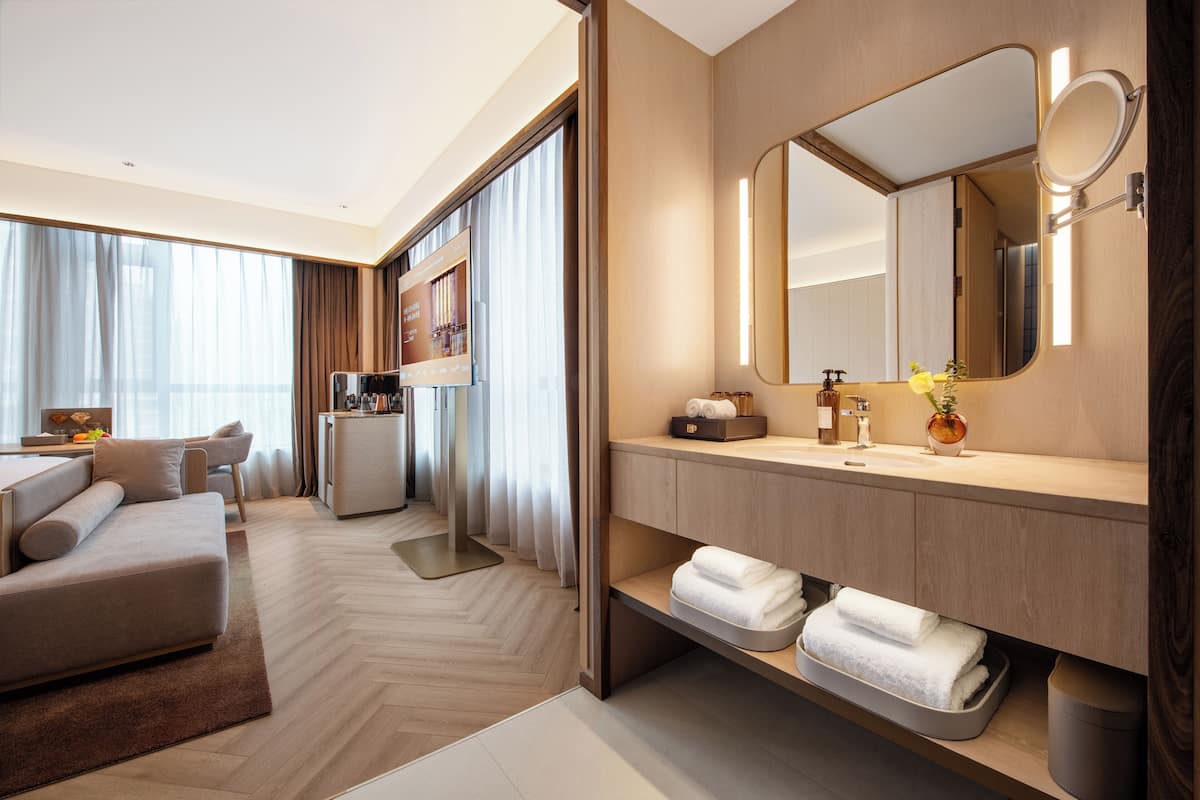 A modern hotel room with a sofa, a vanity with a mirror, and a minibar.