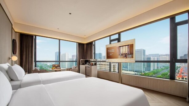 Habitación de hotel con dos camas, televisión, escritorio y vista a la ciudad.