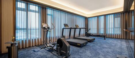 A hotel room with a large window, a treadmill, an elliptical machine, and a small table with a vase.