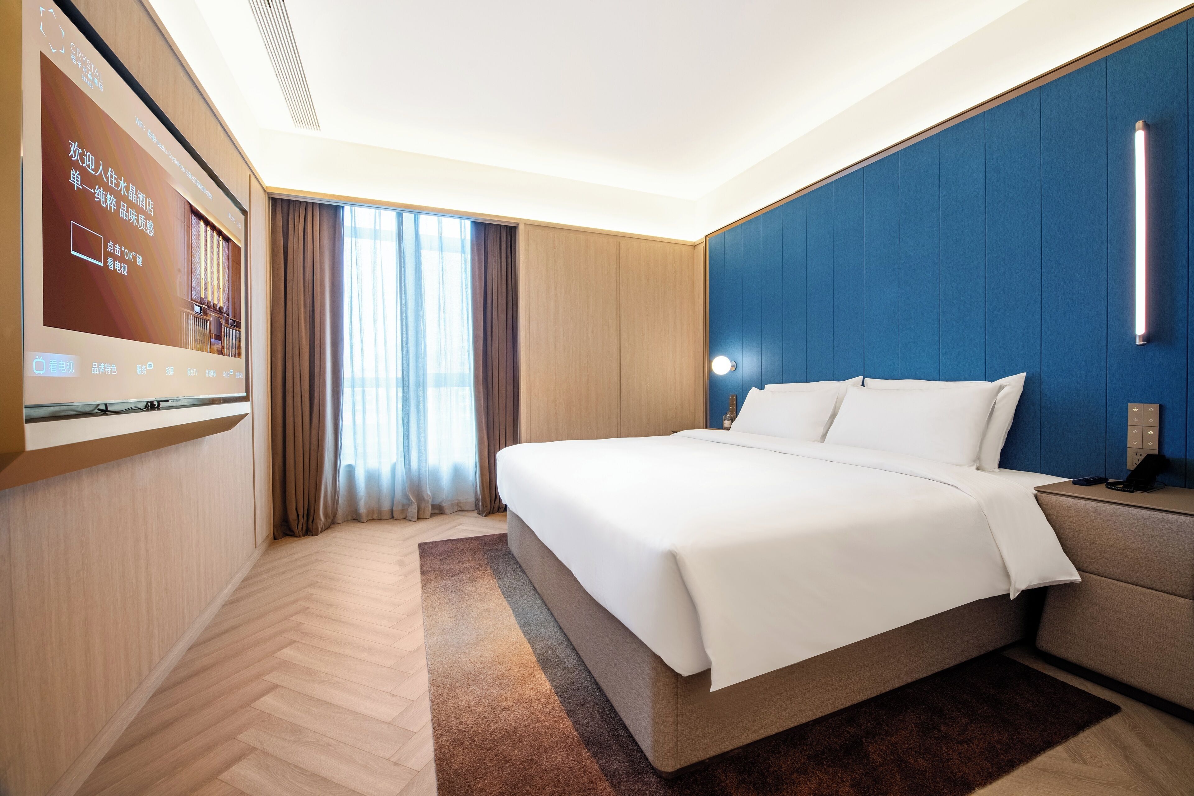 A hotel room with a bed, a TV, a desk, and a window with curtains.