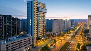 Un edificio de gran altura con varios pisos, rodeado de otros edificios y una calle concurrida con tráfico.