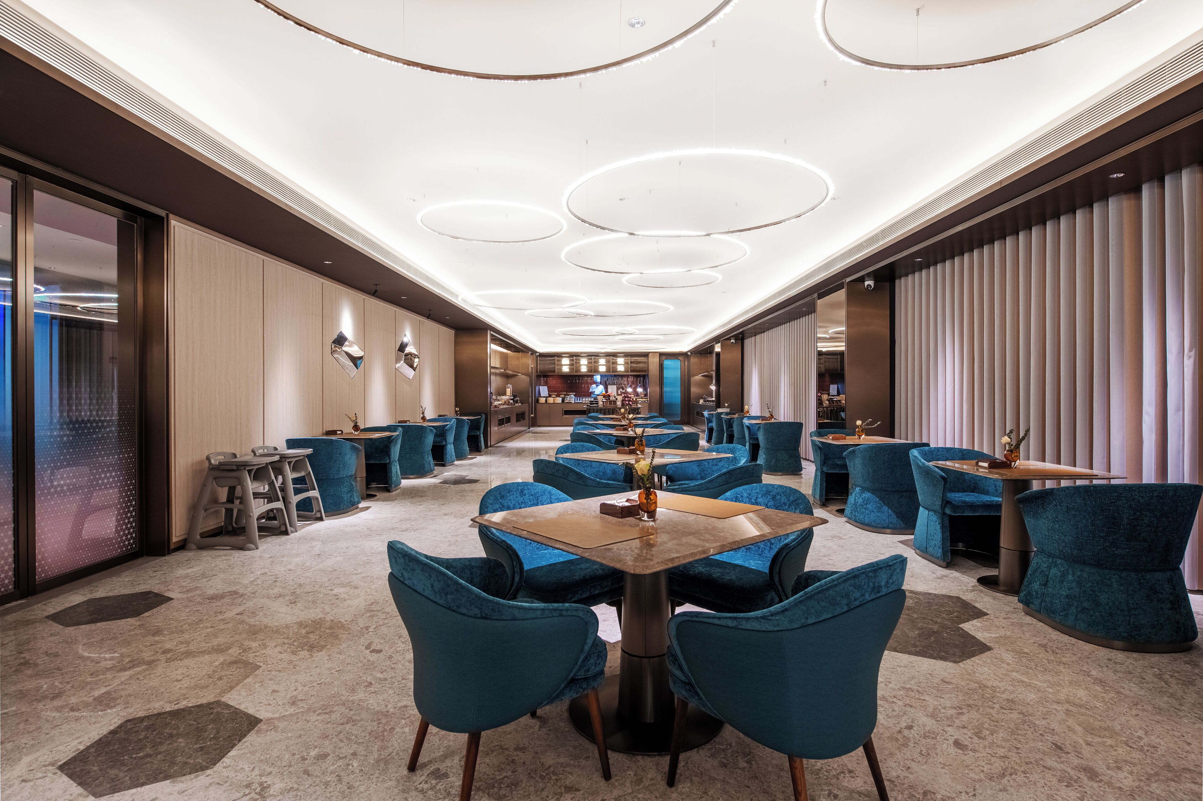 Un comedor de hotel con mesas redondas, sillas tapizadas en azul y un diseño de techo moderno.