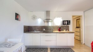 A modern kitchen with white cabinets, a stainless steel range hood, a microwave, and a red kettle. - Alta Rocca - ALATA - Gîte (ALATA)
