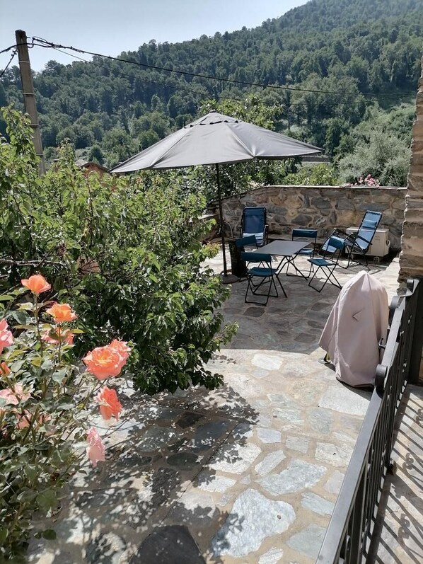 A stone patio with outdoor seating, a covered table, and a view of a forested hillside. - U Rataghju - LA PORTA (LA PORTA)