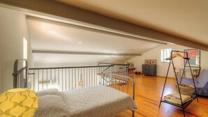 Une chambre aménagée en mezzanine comprenant un lit, un fauteuil suspendu, un coin repas et un escalier.