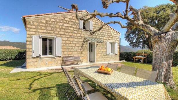 Une maison en pierre avec un patio, une table et des chaises, et un panier de fruits.