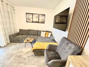 Ein Wohnzimmer mit grauem Sofa, einem Holztisch und einer gelben Decke.