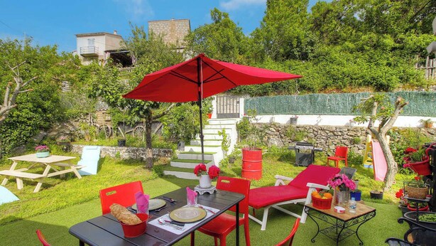Eine Terrasse mit Gartenmöbeln, einem roten Sonnenschirm und einer Steinmauer.