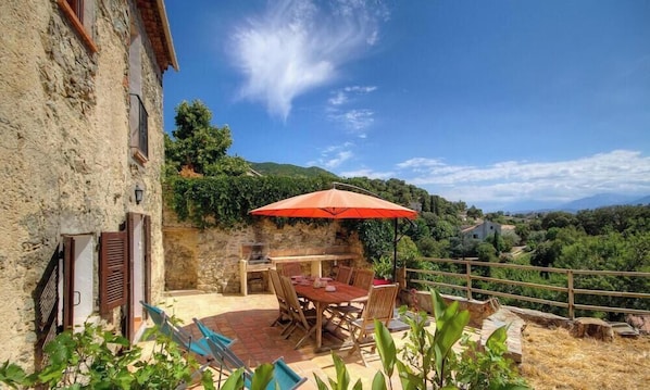 Ein Steinhaus mit Terrasse, einem Tisch, Stühlen und einem Grill.