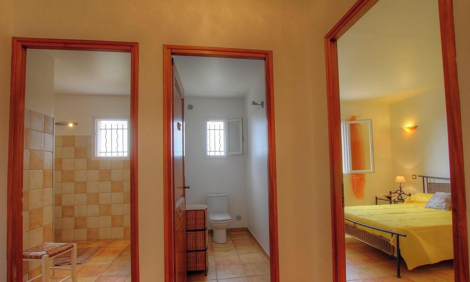 Una habitación con una cama, un baño con inodoro y ducha, y un pasillo.