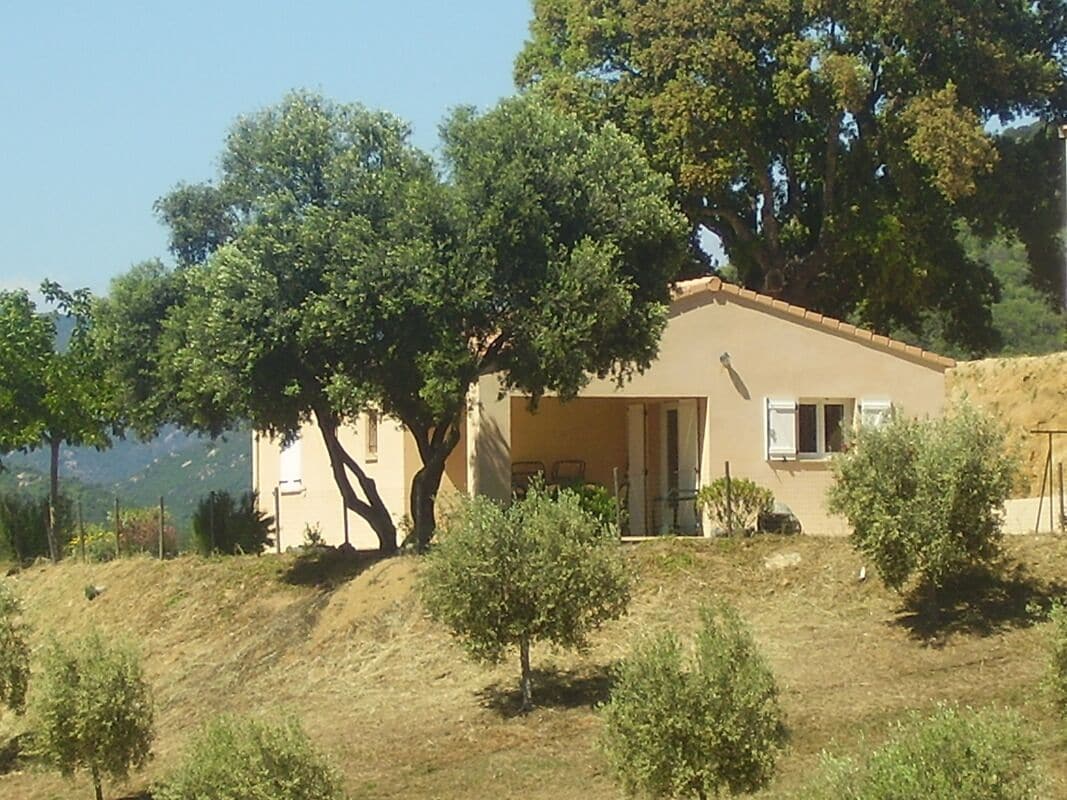 Ein eingeschossiges Gebäude mit flachem Dach, umgeben von Bäumen und einer hügeligen Landschaft.