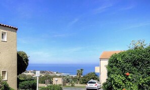 A coastal residential area with a view of the sea, a car parked in the foreground, and a building with a red roof. - Le 165 - LUMIO - Gîte (LUMIO)