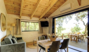 Ein Holzinnenraum mit einer Couch, einem Tisch mit Stühlen, einem Fernseher und einem großen Fenster.