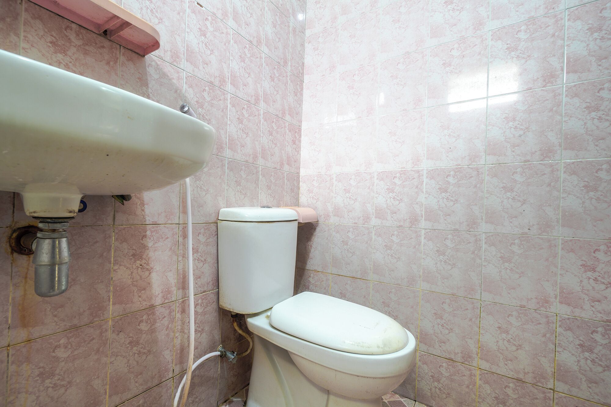 Un baño con inodoro, lavamanos y azulejos de mármol rosa.
