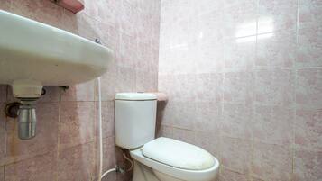Un baño con inodoro, lavamanos y azulejos de mármol rosa.