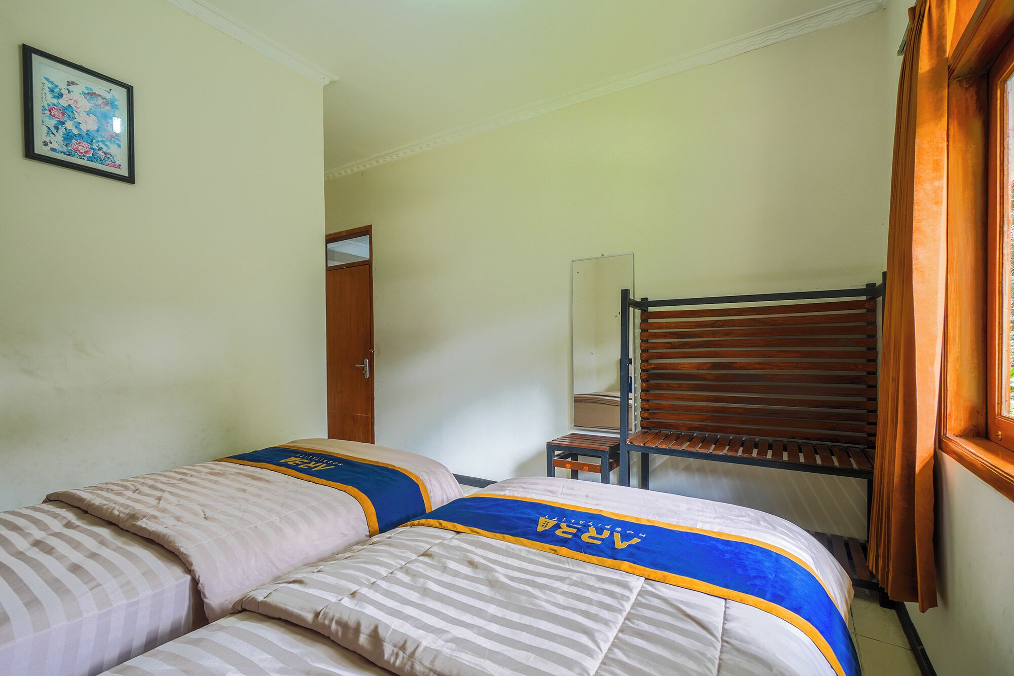 A room with two beds, a wooden bench, a door, and a framed picture on the wall.
