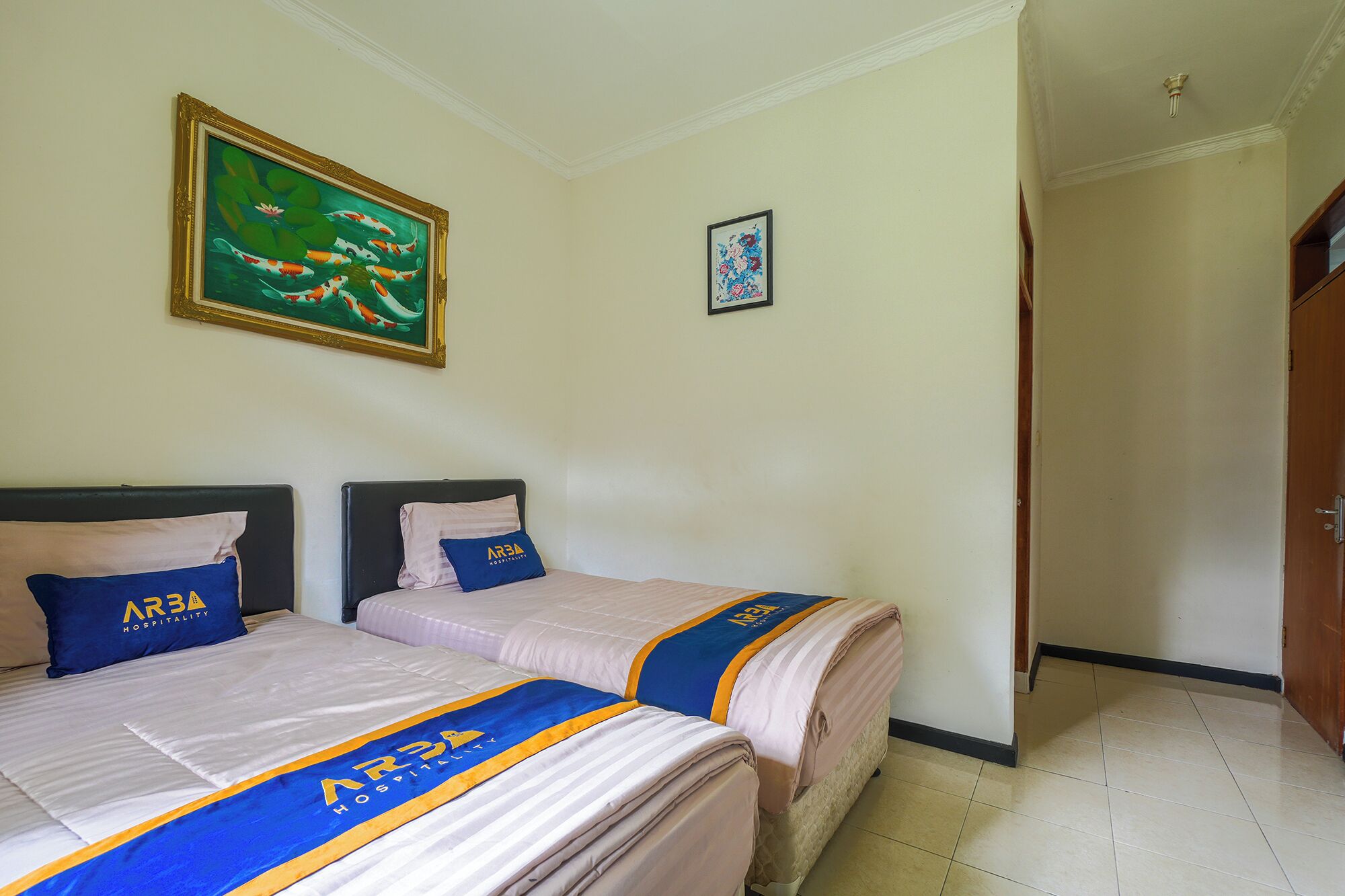 A hotel room with two beds, a painting of koi fish, and a framed floral artwork.