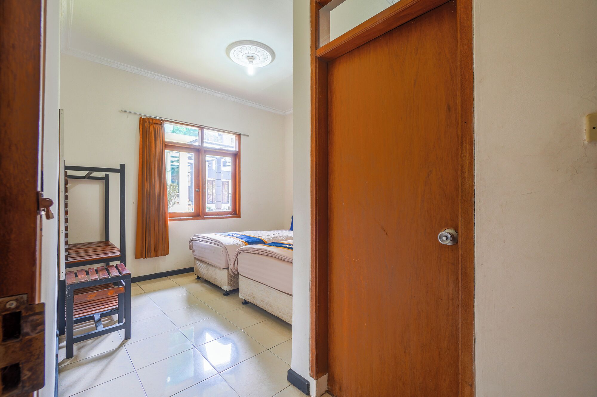 A room with a bed, a wooden door, a window with curtains, and a metal rack.