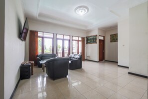 Ein geräumiger Raum mit großem Fenster, einem Flachbildfernseher, zwei Ledersofas, einem kleinen Tisch und einer Tür zu einem weiteren Raum.
