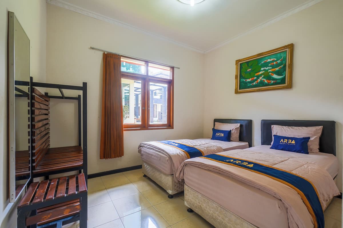 A hotel room with two beds, a window with curtains, a painting, and a wooden rack.