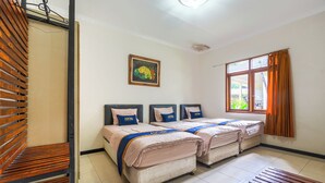 Une chambre d’hôtel avec deux lits, une fenêtre avec des rideaux, un tableau au mur et un banc en bois.