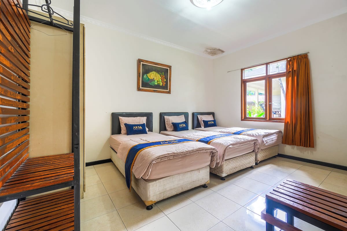 A hotel room with two beds, a window with curtains, a painting on the wall, and a wooden bench.