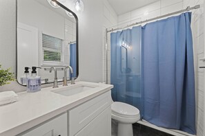 Een badkamer met een wit wastafelmeubel, een spiegel, een toilet en een blauw douchegordijn.