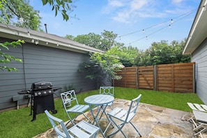 Ein Garten mit Grill, rundem Tisch und Stühlen.