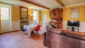 Un coin repas avec une table dressée pour quatre personnes, un buffet en bois et un téléviseur, le tout dans une pièce aux murs jaunes et aux poutres apparentes.