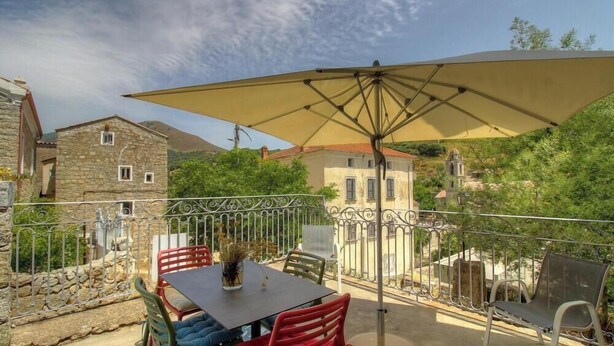 Une terrasse extérieure avec une table et des chaises, un grand parasol et un bâtiment en pierre en arrière-plan.