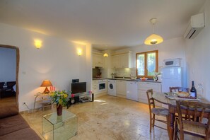 A compact living space with a kitchenette, a dining area, and a seating area with a TV and lamp. - Casa Pachjola - URTACA (URTACA)