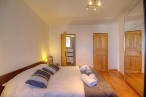 A bedroom with a bed, a wooden wardrobe, a mirror, and a door leading to a bathroom. - Casa Pachjola - URTACA (URTACA)