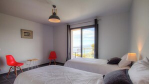 Ett hotellrum med två sängar, en röd stol, ett litet bord, ett fönster med utsikt och en hängande lampa.