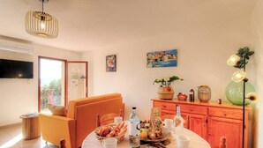 Un coin repas avec une table dressée pour deux personnes, un canapé, un meuble en bois agrémenté d’objets décoratifs et un téléviseur fixé au mur.