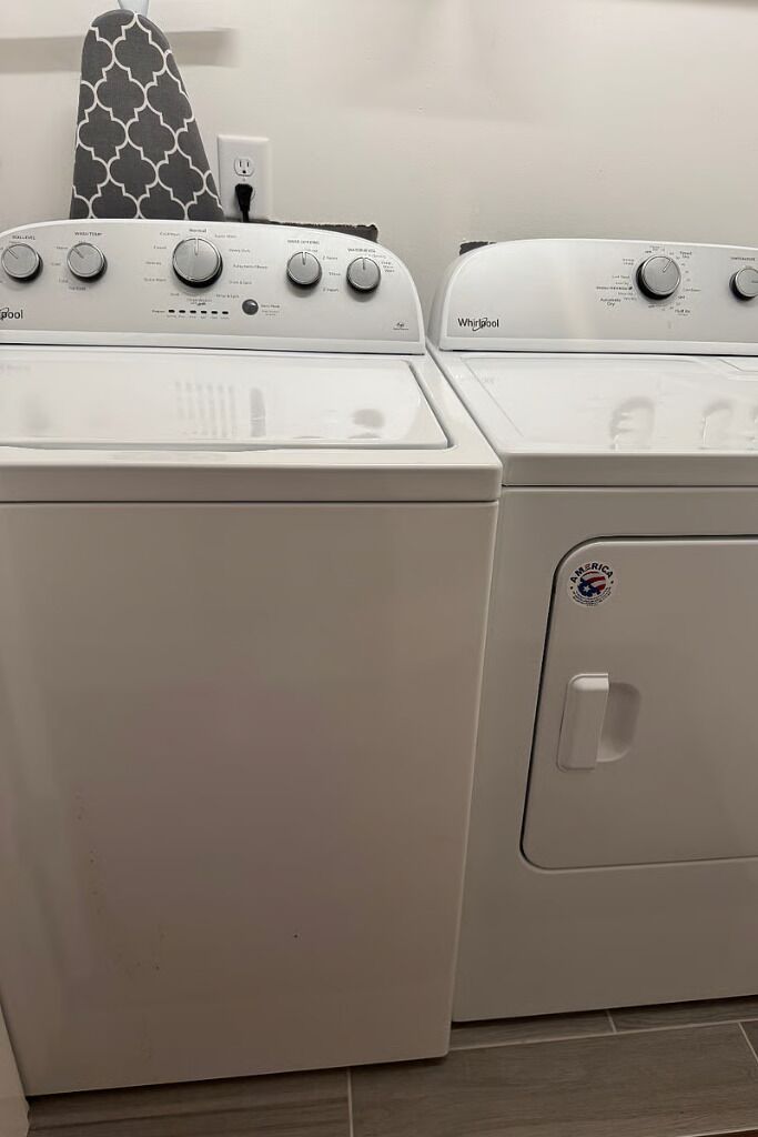 Twee voorladers van Whirlpool, met een gestreept strijkplank erboven.