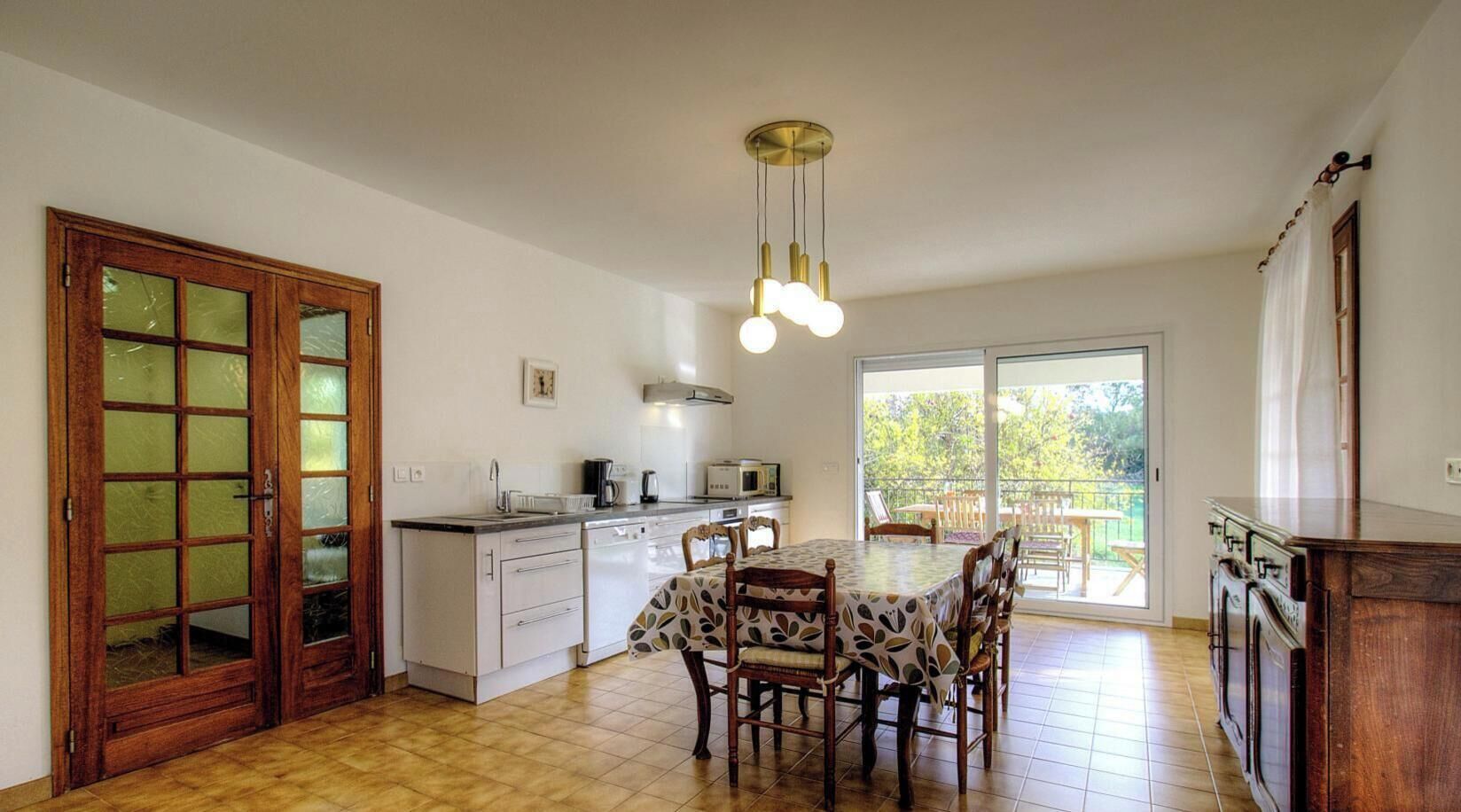 Une cuisine avec un coin repas, une grande fenêtre et un luminaire au plafond.