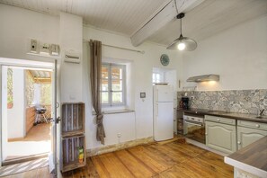 Eine Küche mit Holzboden, einem Fenster mit Vorhängen, einem Kühlschrank, einem Herd und einem Spülbecken.