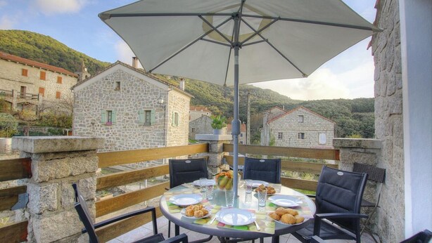 A table set outdoors with a large umbrella, surrounded by stone buildings and a mountainous backdrop. - Christina - CASALABRIVA (CASALABRIVA)