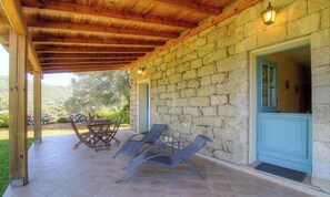 A stone building with a covered patio, outdoor seating, and a door with a blue frame. - Les oliviers 2 - SOLLACARO (SOLLACARO)