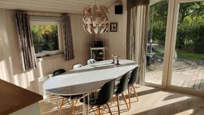 Een eethoek met een grote tafel, stoelen, een hanglamp en uitzicht op het buitengebied.