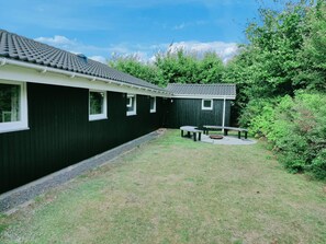 A building with a dark exterior, a tiled roof, and a small outdoor seating area with benches and a table. - 4 Star Holiday Home in Hemmet (Hemmet)