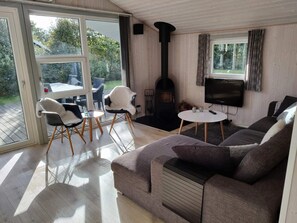 Ein Wohnzimmer mit einer Couch, einem Fernseher, einem Kamin und einer Glastür, die zu einem Außenbereich führt.