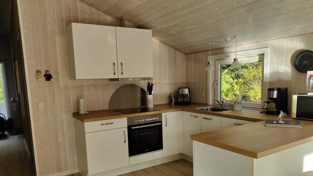 Een moderne keuken met houten kastjes, een vaatwasser, een koffiezetapparaat en een klok aan de muur.