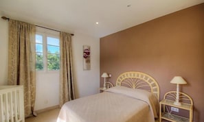 Ein Schlafzimmer mit einem Bett, zwei Nachttischen, einem Fenster mit Vorhängen und einer Wandlampe.