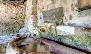 A stone structure with a water feature, possibly a fountain, and a hole in the stone. - Tilleul 5 - COSTA - Gîte (COSTA)